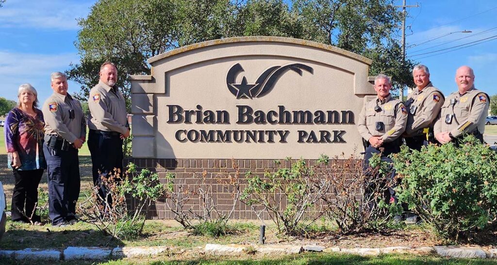 Members of the Brazos County Precinct 1 Constable's office posing with the sign for Brian Bachmann Community Park.