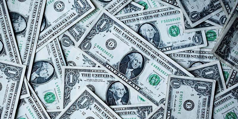 Promo image for the Taxes section of the website. Image of individual dollar bills scattered on top of each other in a pile.