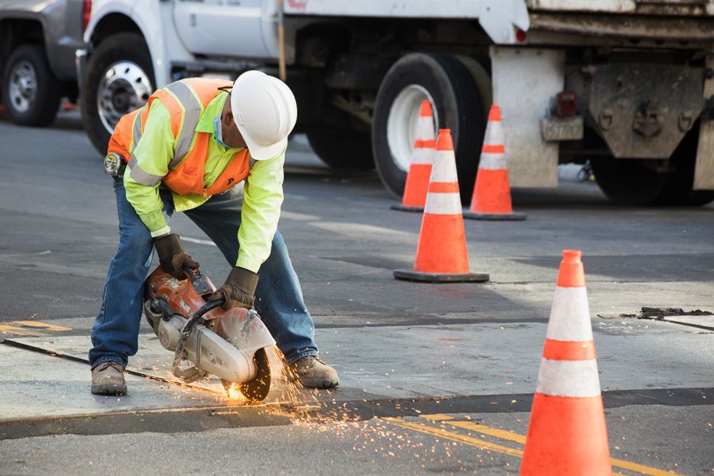 A worker uses a concrete saw to open up part of a street.