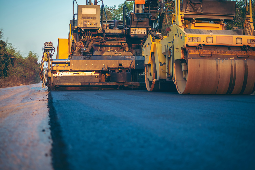 a paver rolls and presses new asphalt on a rural road.